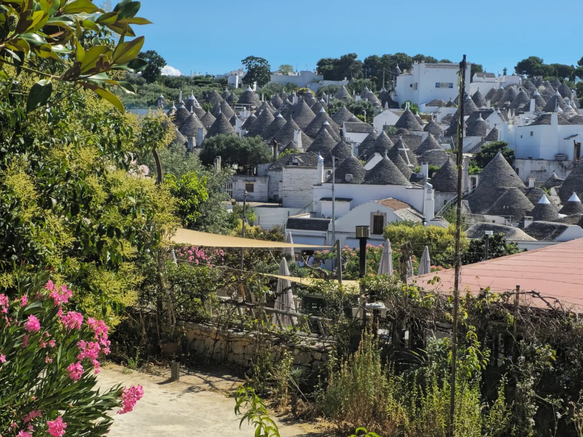 Charming view of traditional Trulli houses in Alberobello, Italy, surrounded by lush greenery under a clear blue sky.